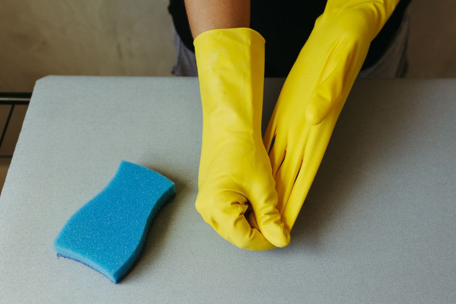 Close-up of hands in yellow gloves preparing for cleaning with blue sponge.
